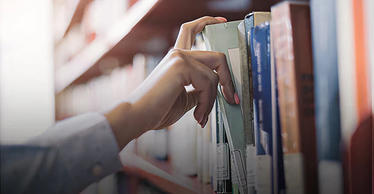 Close-up of a hand reaching for a green book on a library shelf